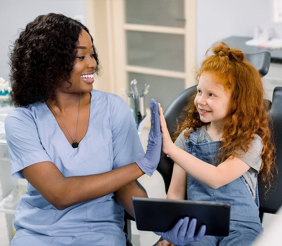 Healthcare provider and young child smile while sharing a high-five.