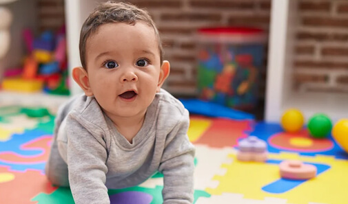 Smiling baby crawls on a colorful play mat.