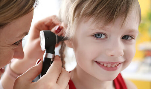 Healthcare provider examines a smiling child’s ear with an otoscope.