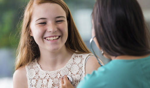 Healthcare provider listens to a smiling teen’s heartbeat with a stethoscope.