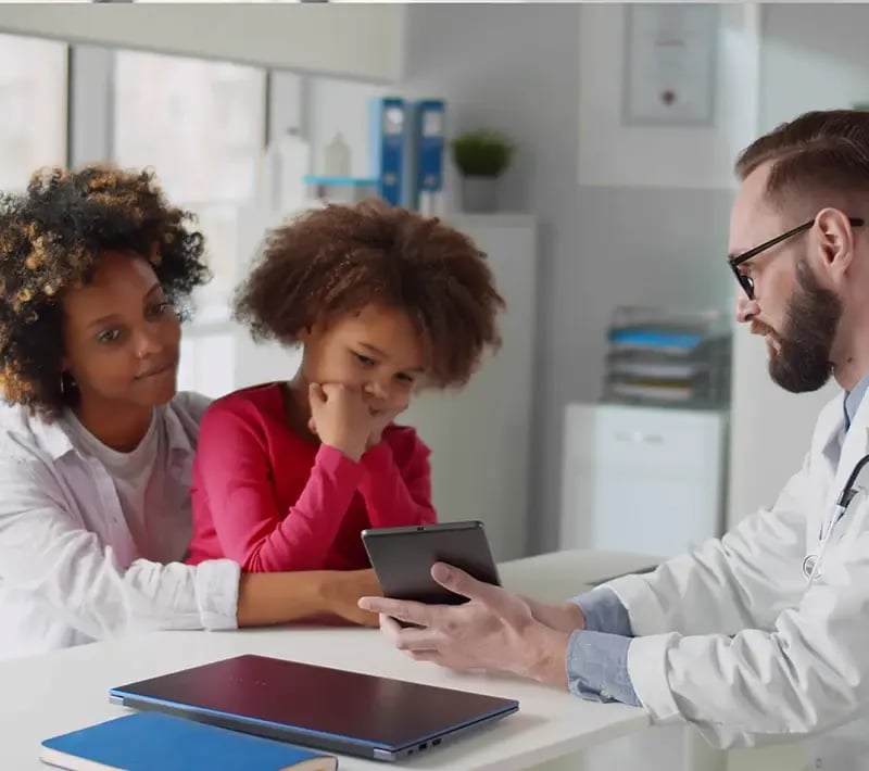 Doctor shows a tablet to a child and parent during a medical visit.