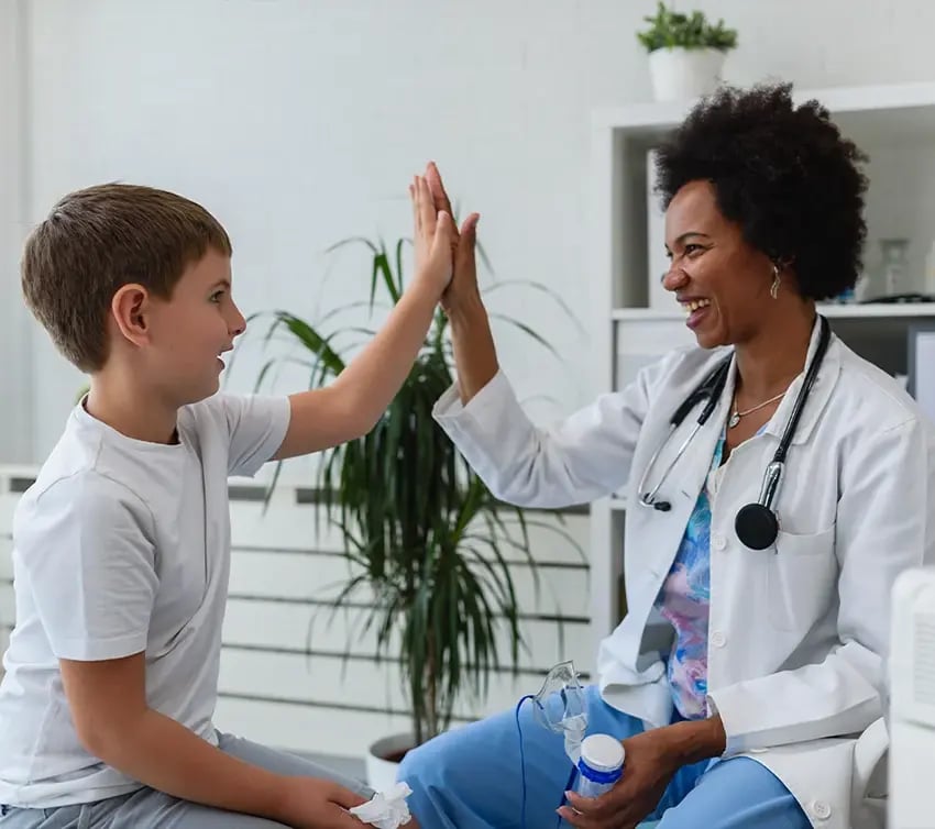 Pediatrician and young patient smile while sharing a high-five during a visit.
