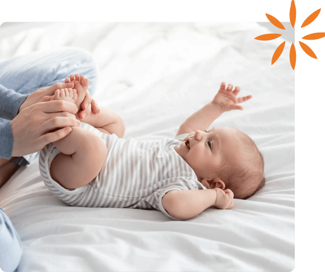 Parent gently holding and playing with a smiling baby on a bed.