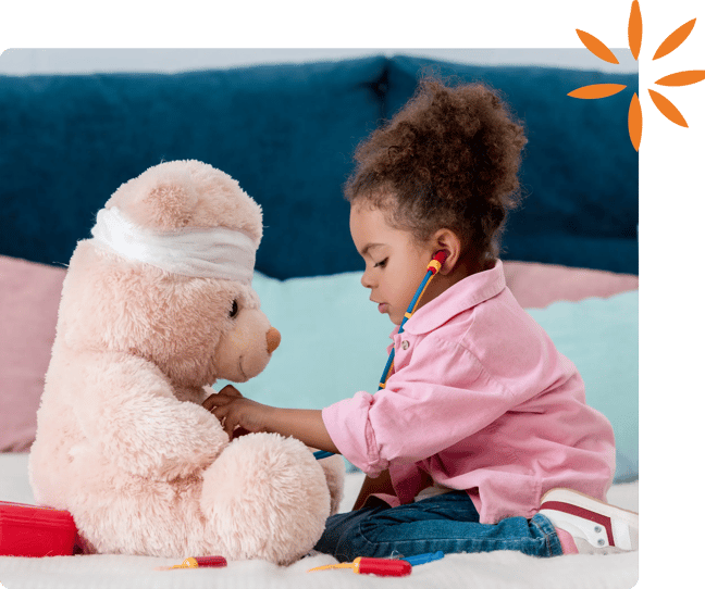 Child uses a toy stethoscope to examine a teddy bear with a bandaged head.