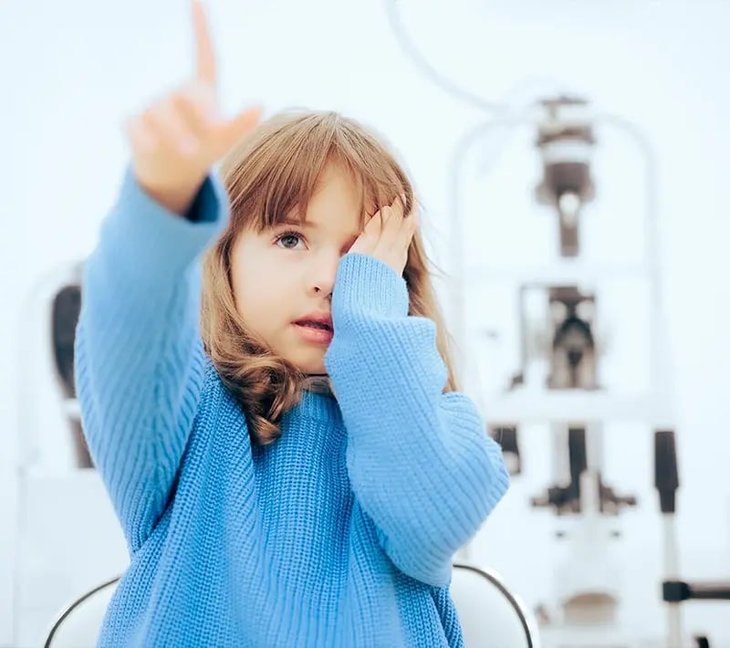 Young child covers one eye and points upward during a vision screening.