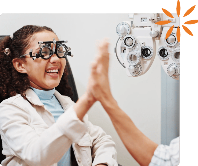 Smiling child wearing eye exam lenses high-fives an eye care provider during a vision test.