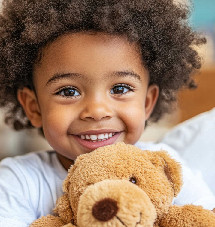 Smiling young child hugs a teddy bear and looks at the camera.