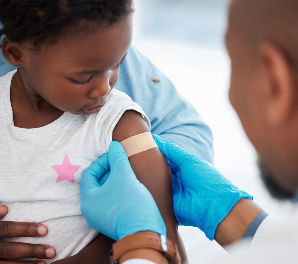 Healthcare provider places a bandage on a young child’s arm after a vaccination.